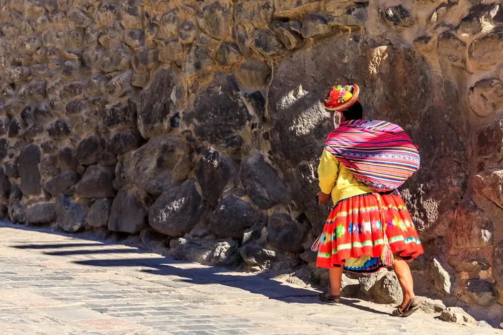A woman in Peru carrying a bundle along an old stone wall