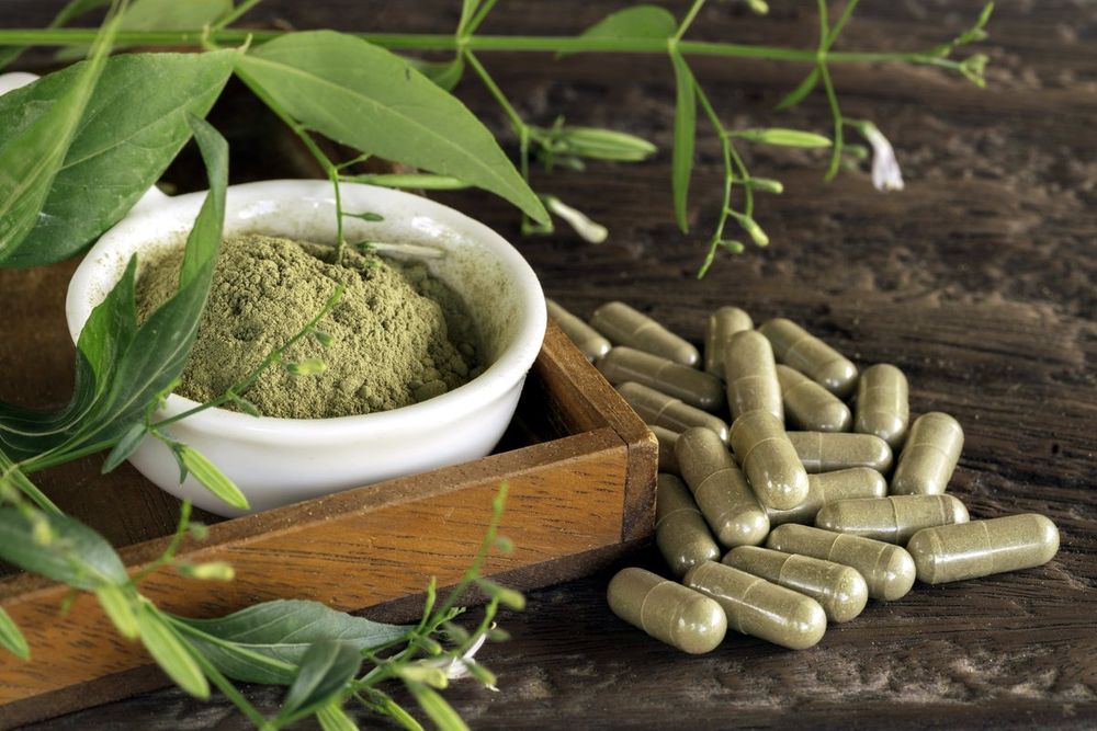 Capsules beside dried herb in a wooden tray