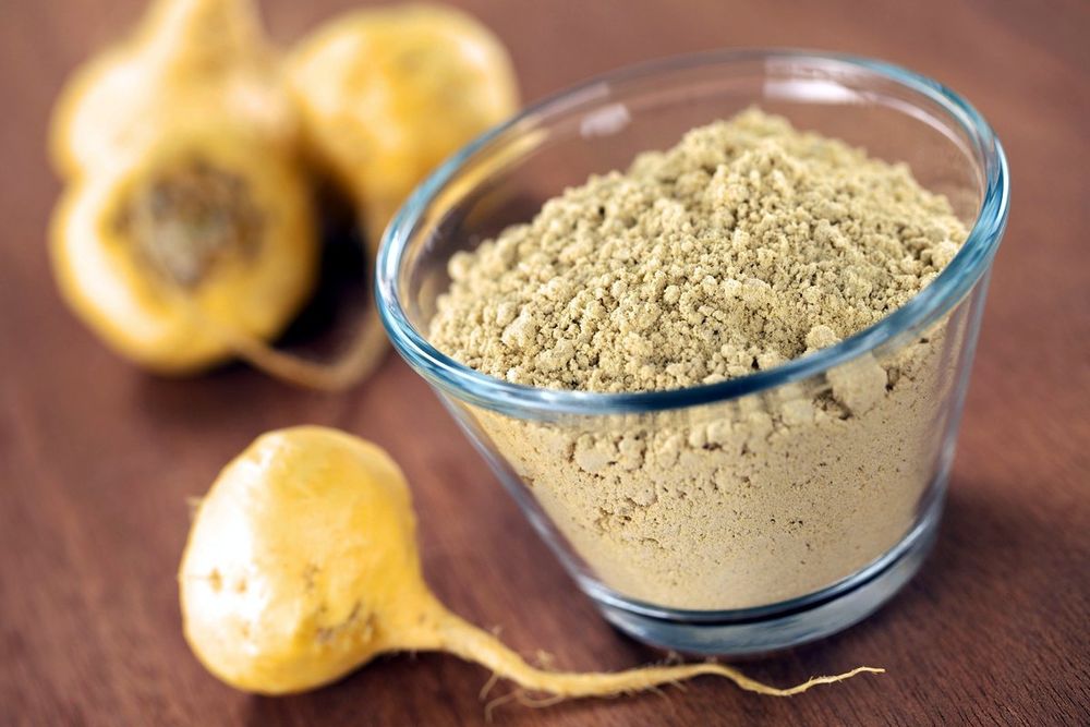 Maca roots beside a glass bowl of ground maca